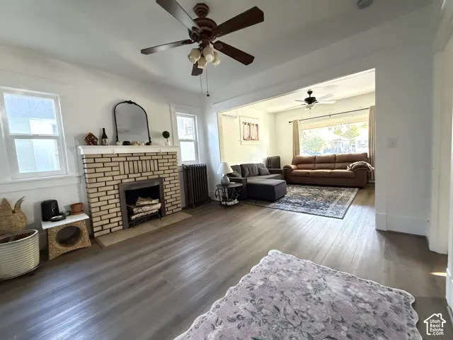 Wood-finish flooring throughout, featuring a brick-clad fireplace, ceiling fans with integrated lighting, and multiple windows