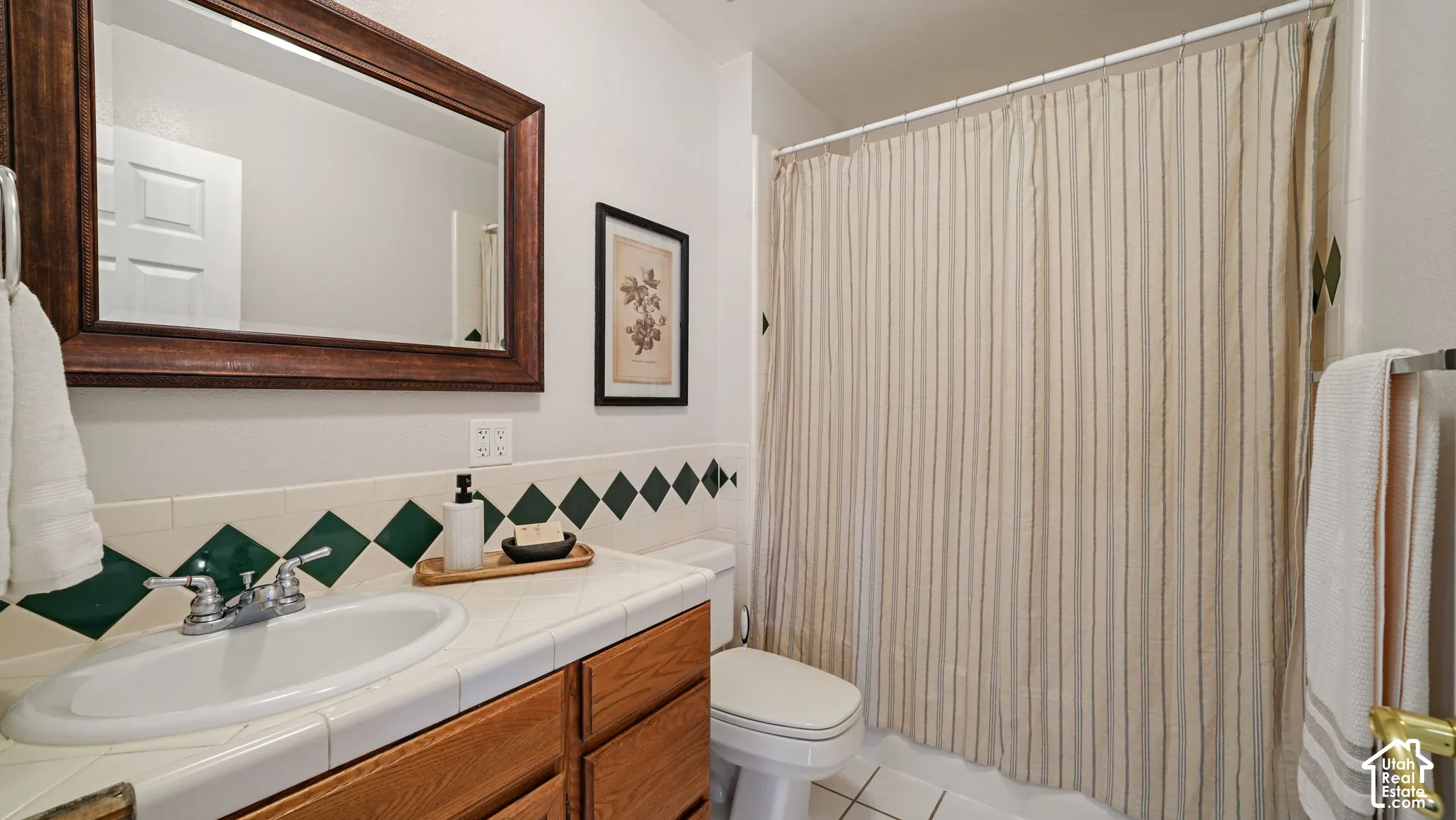 Hardwood vanity with a drop-in sink, chrome faucet, tiled countertop, and wood-framed mirror