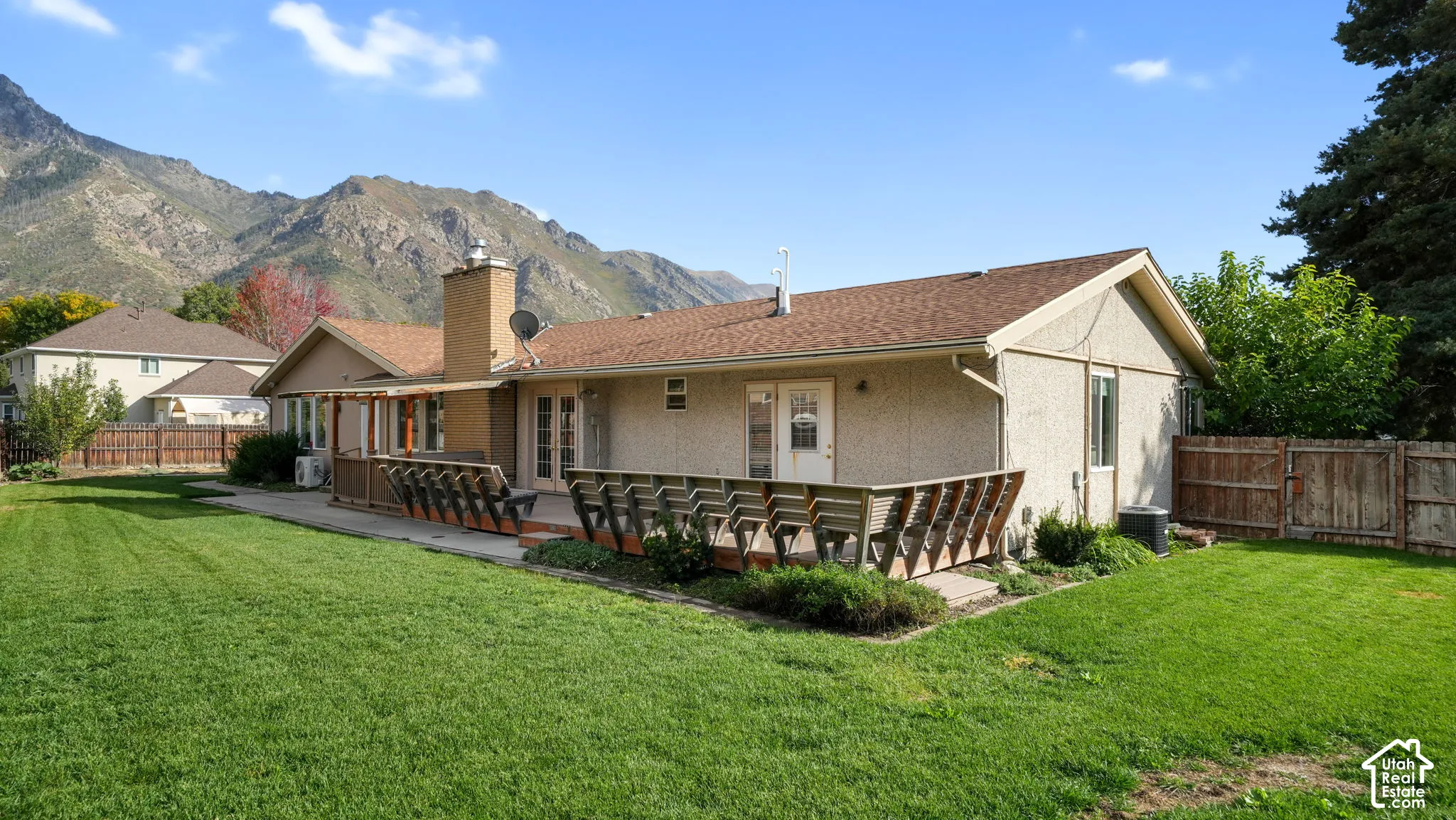 Expansive backyard featuring a large wood deck, stucco exterior, and a chimney