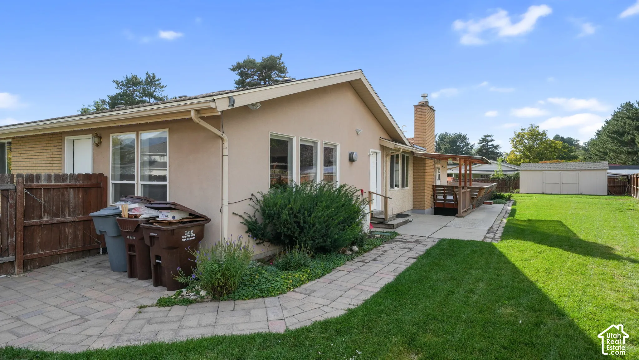 Expansive backyard featuring a manicured lawn, paved patio, and a wooden deck