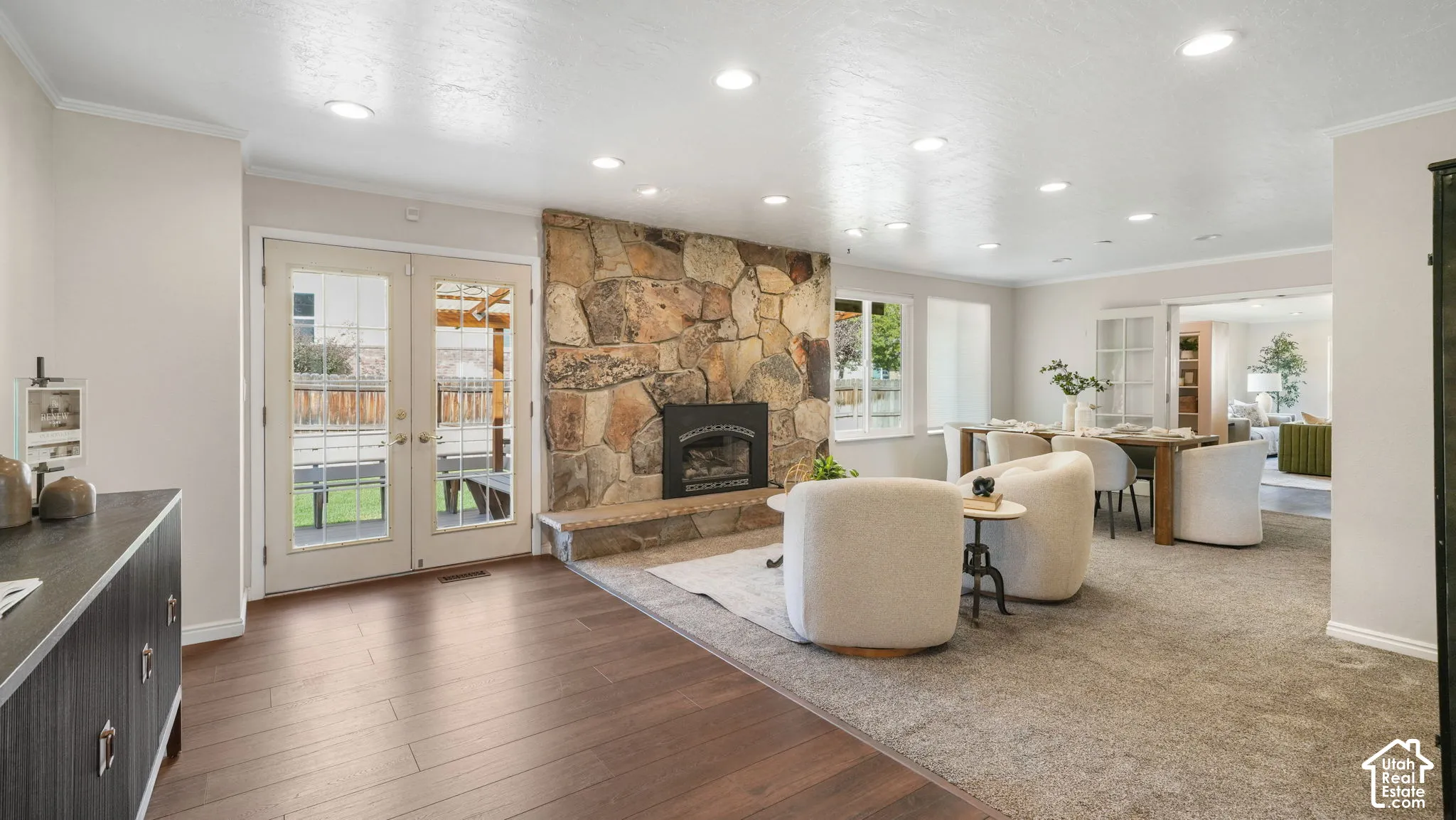 Stone-clad fireplace with hearth, recessed lighting, wood-finish flooring, and French doors leading to a paved patio