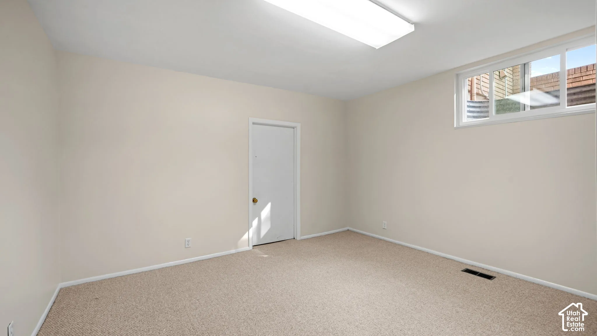 Bright room featuring neutral-toned carpet, a window, and overhead fluorescent lighting