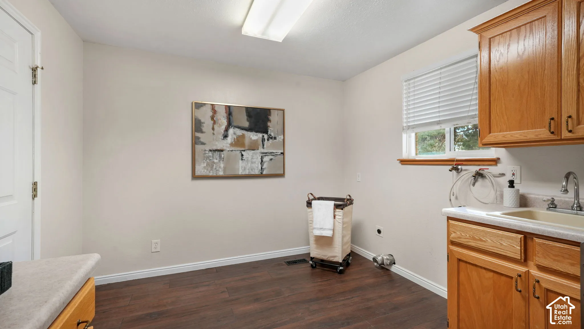 Wood-finish flooring, light tone wall paint, window with blinds, base cabinetry with integrated sink, and overhead cabinetry