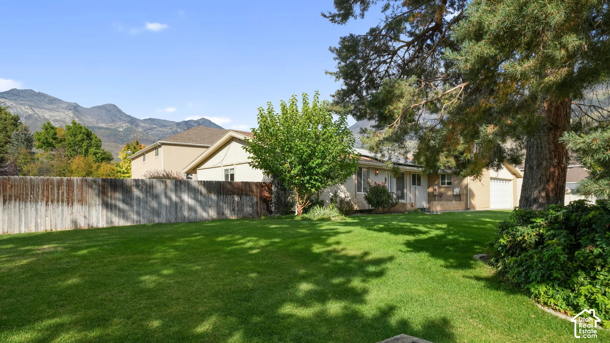 Expansive green lawn with mature trees and a wooden privacy fence, set against a mountain backdrop