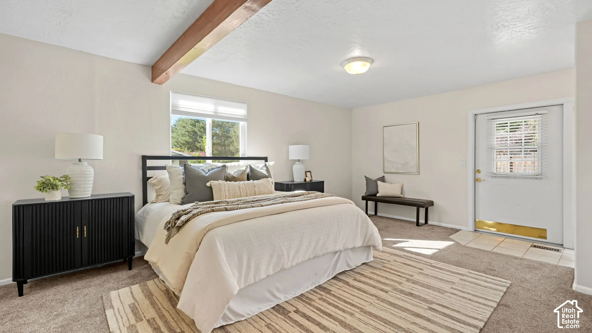 Exposed wood ceiling beam, neutral wall color, window with natural light, wall-mounted light fixture, and exterior access door