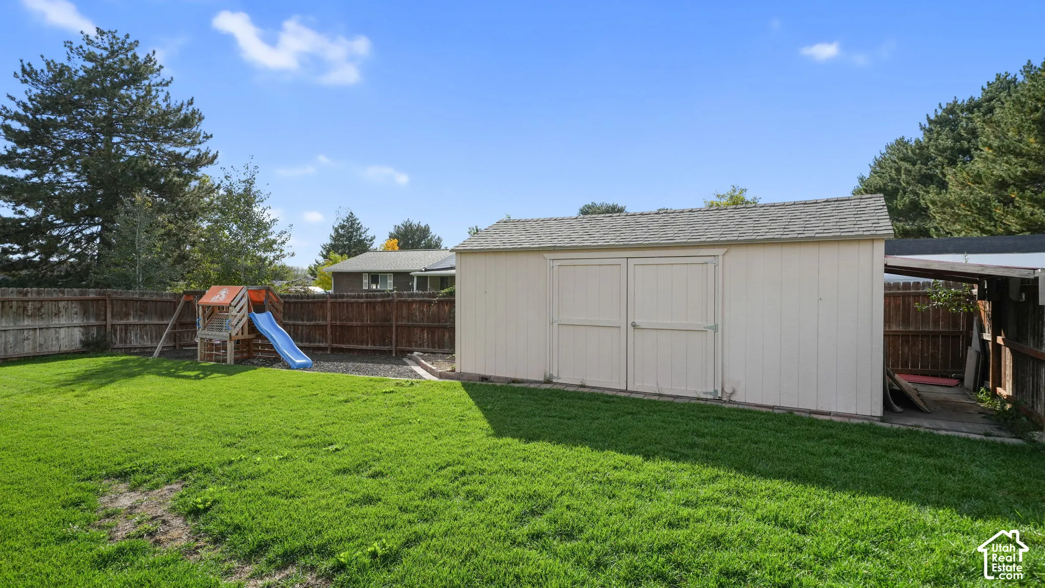 Expansive fenced backyard featuring a grassy lawn, a storage shed with double doors, and an attached covered lean-to