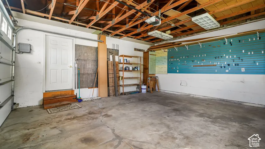 Attached garage with a roll-up door, exposed ceiling joists, and a built-in shelving unit