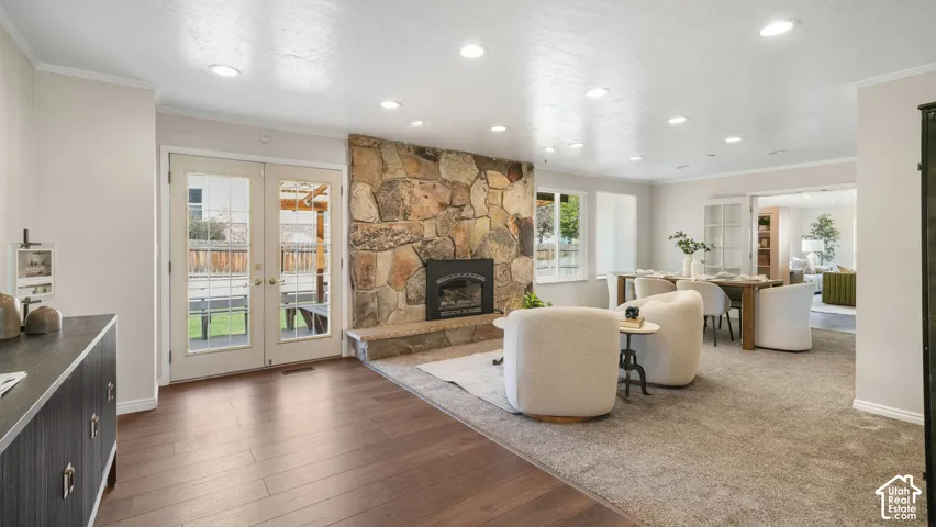Stone-clad fireplace with hearth, recessed lighting, wood-finish flooring, and French doors leading to a paved patio