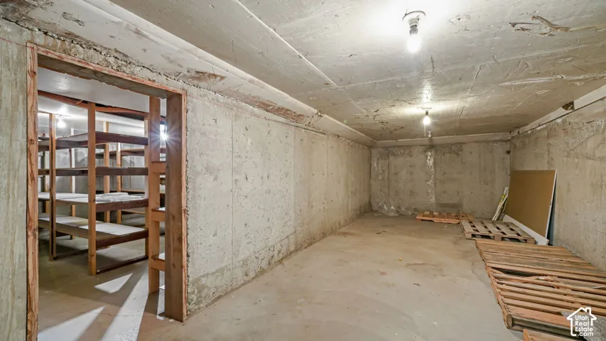 Concrete flooring and walls, accompanied by a separate storage area featuring wooden shelving