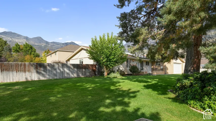 Expansive green lawn with mature trees and a wooden privacy fence, set against a mountain backdrop