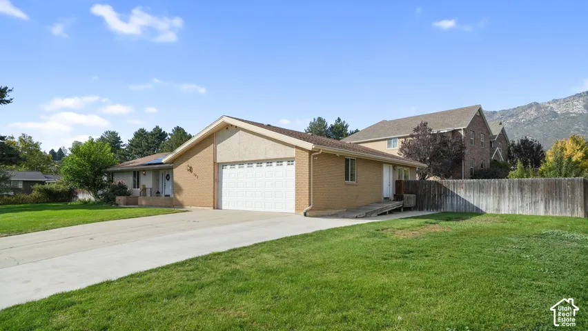 Brick exterior, concrete driveway, attached garage, sloped front yard, and a wooden privacy fence