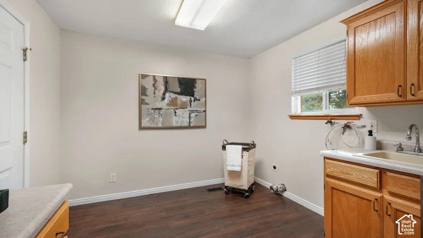 Wood-finish flooring, light tone wall paint, window with blinds, base cabinetry with integrated sink, and overhead cabinetry