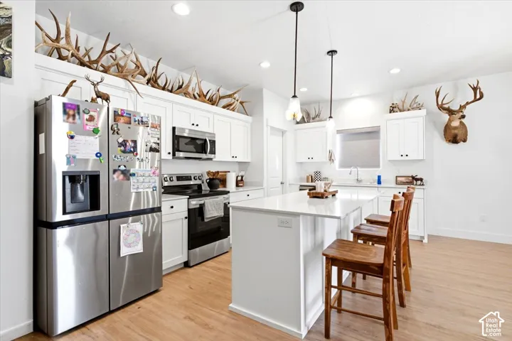 White cabinetry with matte black hardware, stainless steel appliances, wood-finish flooring, and a central island with pendant lighting
