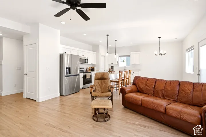 Open-concept interior featuring wood-finish flooring, white cabinetry, stainless steel appliances, recessed lighting, and a multi-light chandelier