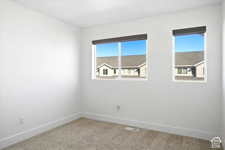 Bright interior with white walls, two windows, gray roller shades, and neutral carpet