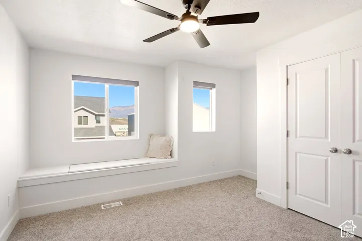 Built-in window seat, dual windows, neutral carpeted flooring, modern dark-finish ceiling fan, and double-door closet