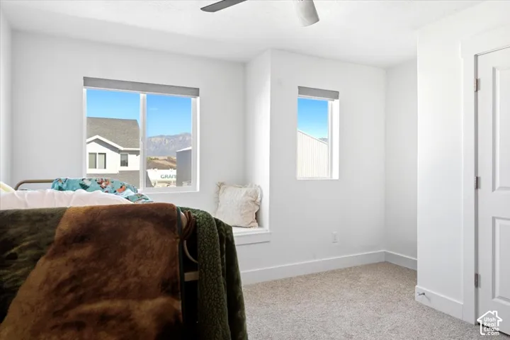 White painted walls and trim, light-colored carpet, a ceiling fan, and a window seat