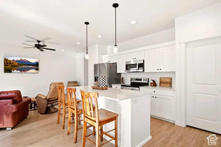 Kitchen featuring white shaker-style cabinetry, quartz countertops, a stainless steel appliance suite, wood-finish flooring, and pendant lighting