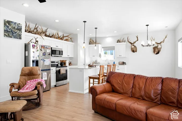 Open-concept living space with wood-finish flooring, recessed lighting, and a kitchen featuring white cabinetry, stainless steel appliances, and a central island with bar seating