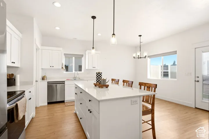 Kitchen featuring a central island with a solid surface countertop, white shaker-style cabinetry, stainless steel appliances, pendant lighting, and wood-finish flooring