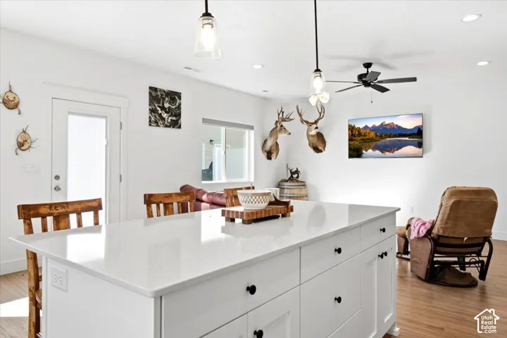 Kitchen island with a white countertop and black hardware, wood-finish flooring, white walls, and recessed lighting