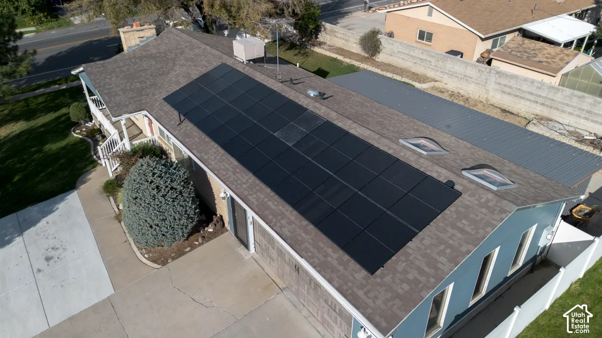 Roof-mounted solar panels, multiple skylights, attached garage, covered front porch, and a white picket fence