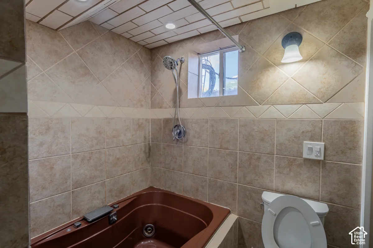 Brown jetted tub with tiled surround, complementary wall tiling, and a window