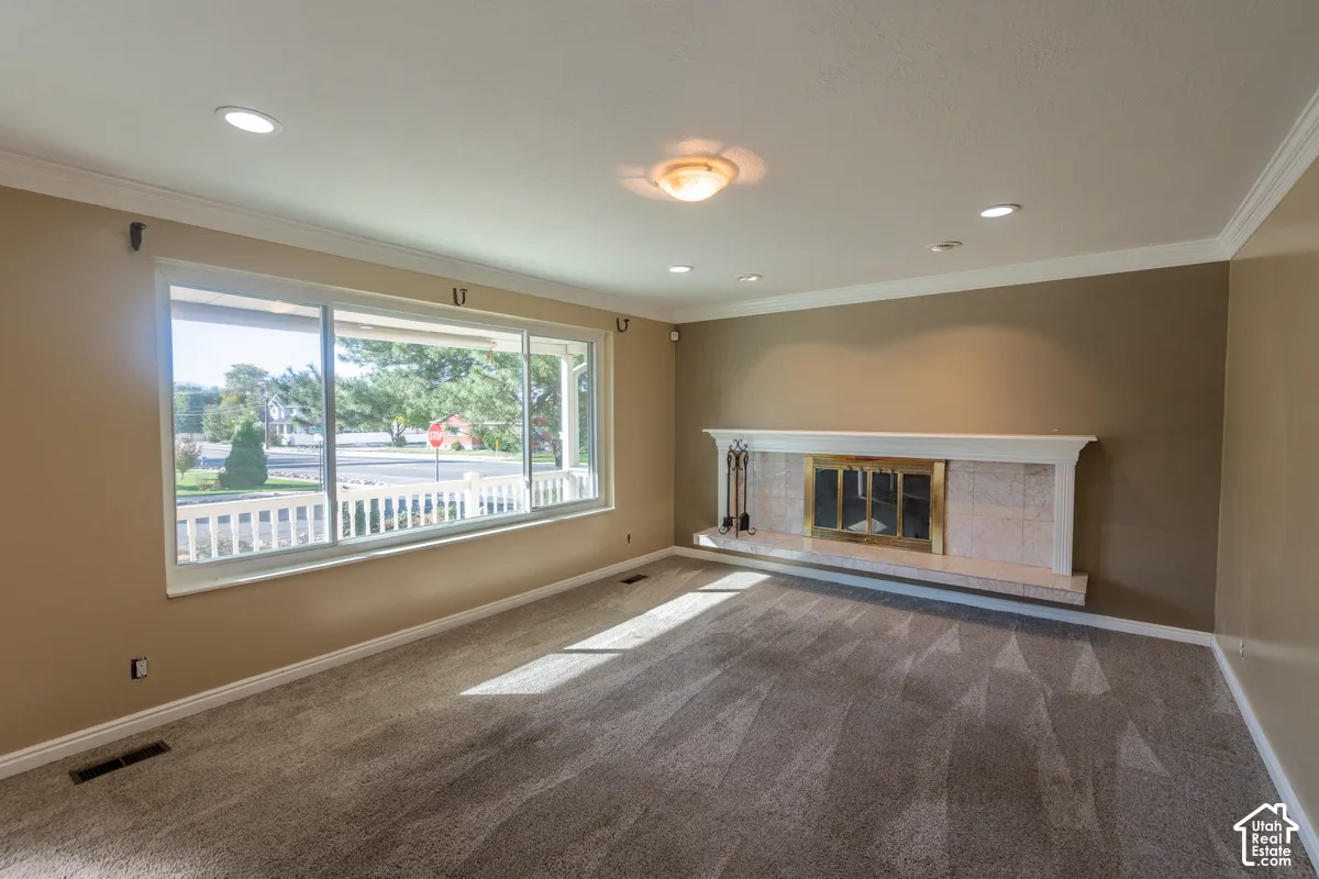 Recessed lighting, crown molding, large picture window, and a fireplace with a tile surround and hearth