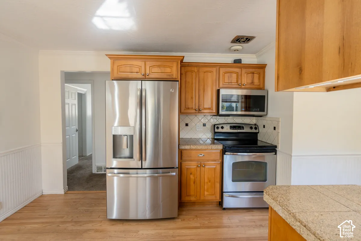 Kitchen featuring stainless steel appliances, wood-finish cabinetry, tile backsplash, and light wood-finish flooring