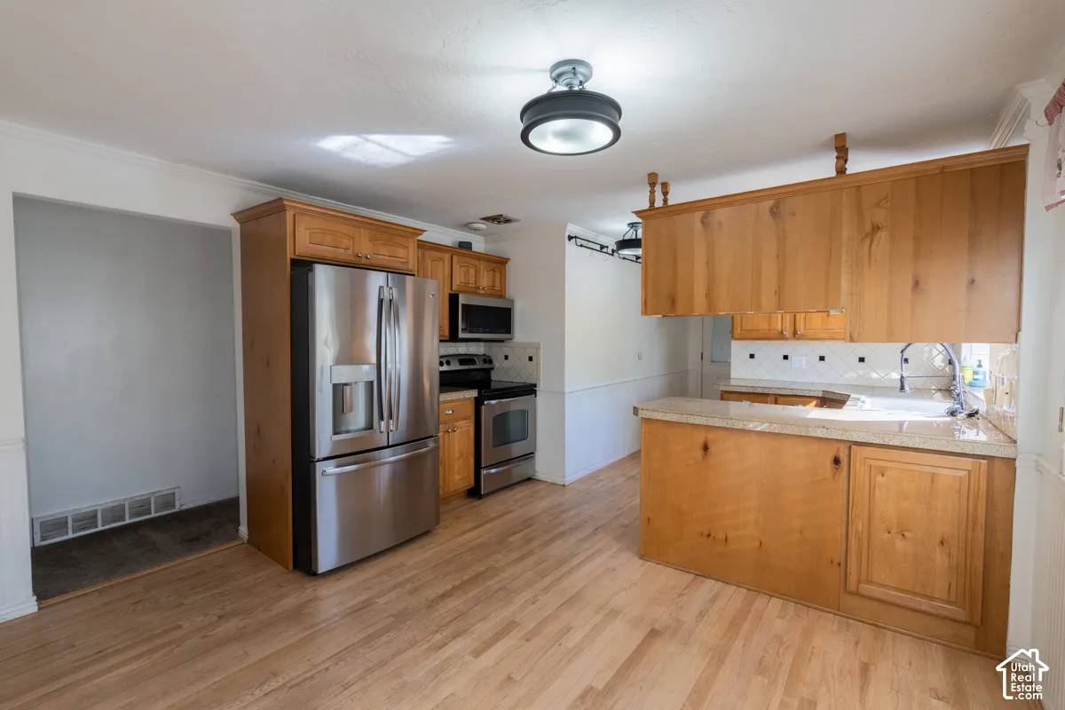 Spacious kitchen featuring wood cabinetry, stainless steel French-door refrigerator, dual wall ovens, wood-finish flooring, and granite countertops with white tile backsplash