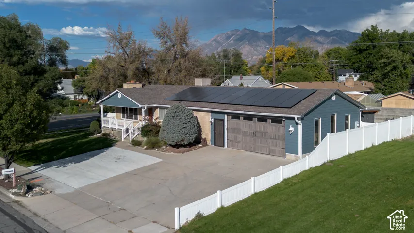 Expansive concrete driveway, two-car garage with wood-finish doors, solar panels, and a white privacy fence