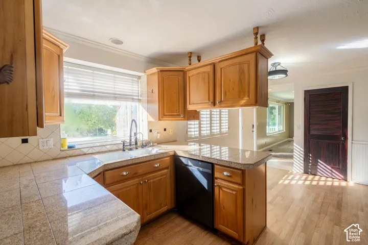 Kitchen with wood cabinetry, tile countertops, tile backsplash, built-in dishwasher, and wood-finish flooring