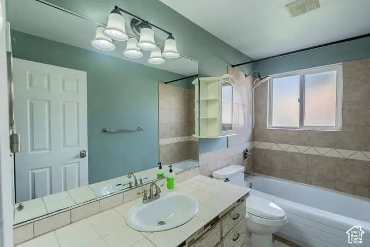 Spa-inspired bathroom featuring a large framed mirror, dual-sink vanity with wood-finish cabinetry, ceramic tile flooring, and subway tile accents