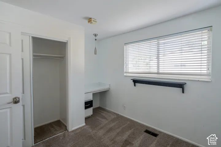 Built-in closet with sliding doors, built-in desk with drawers, overhead light fixture, window with blinds, and wall-mounted shelf