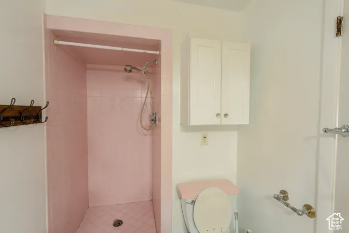 Pink tiled shower stall with wall-mounted showerhead, white wall cabinetry, and chrome towel bars