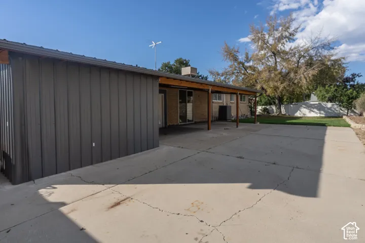 Expansive concrete patio with a covered outdoor area, corrugated metal siding, brick exterior, and a manicured lawn