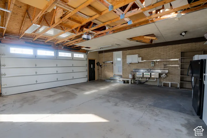 Attached garage featuring a white sectional door with upper transom windows, exposed ceiling joists, concrete flooring, and a utility sink with stainless steel basin