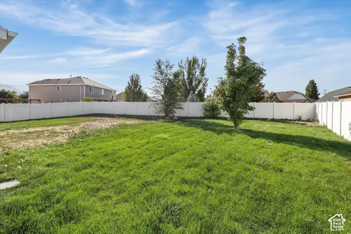 Expansive backyard featuring a lush lawn, mature trees, and a white privacy fence