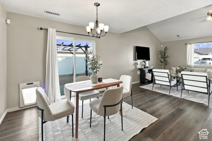Vaulted ceiling over the living area, wood-finish flooring, sliding glass door with access to an exterior pergola, and a dining area with a chandelier