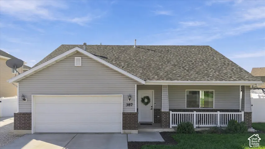 Grey siding exterior with brick accents, attached garage, covered front porch with white railing, asphalt shingle roof, and concrete driveway