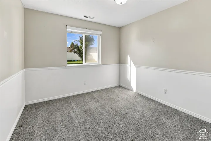 Window with outdoor scenery, neutral-toned walls, white wainscoting, gray carpet, and a ceiling light fixture