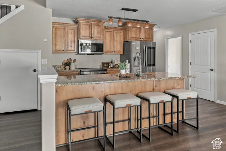 Kitchen featuring wood-finish cabinetry, stainless steel appliances, a multi-tone stone countertop, and wood-finish flooring