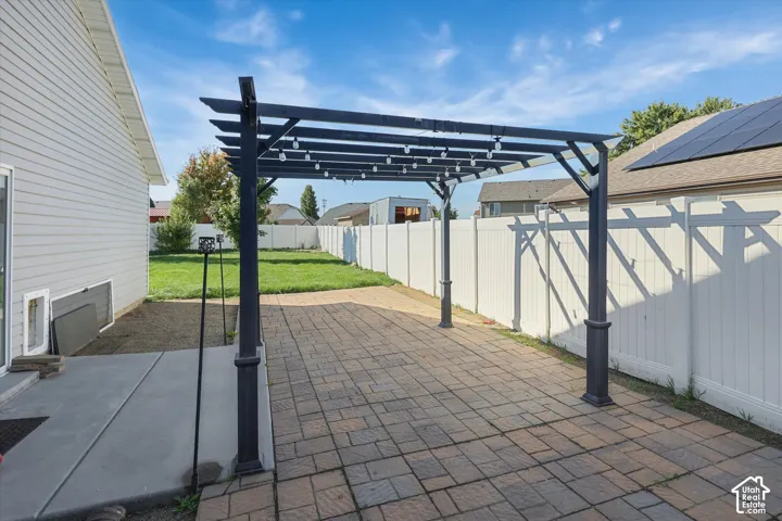 Paver patio with an overhead pergola featuring string lights, a concrete patio extension, a vinyl privacy fence, and a manicured lawn