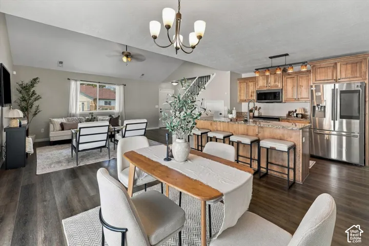 Vaulted ceilings, wood-finish flooring, and a kitchen featuring wood cabinetry, stainless steel appliances, and a breakfast bar with seating