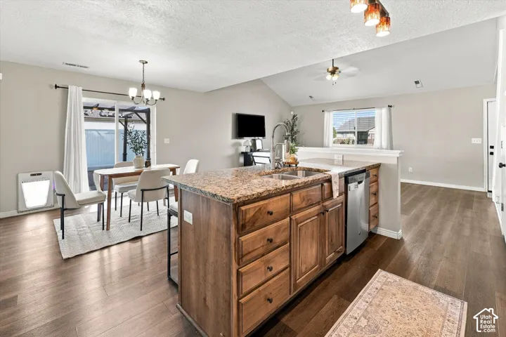 Open-concept living space featuring wood-finish flooring, a kitchen island with stone countertops and an undermount sink, and a dining area with a sliding glass door to the exterior