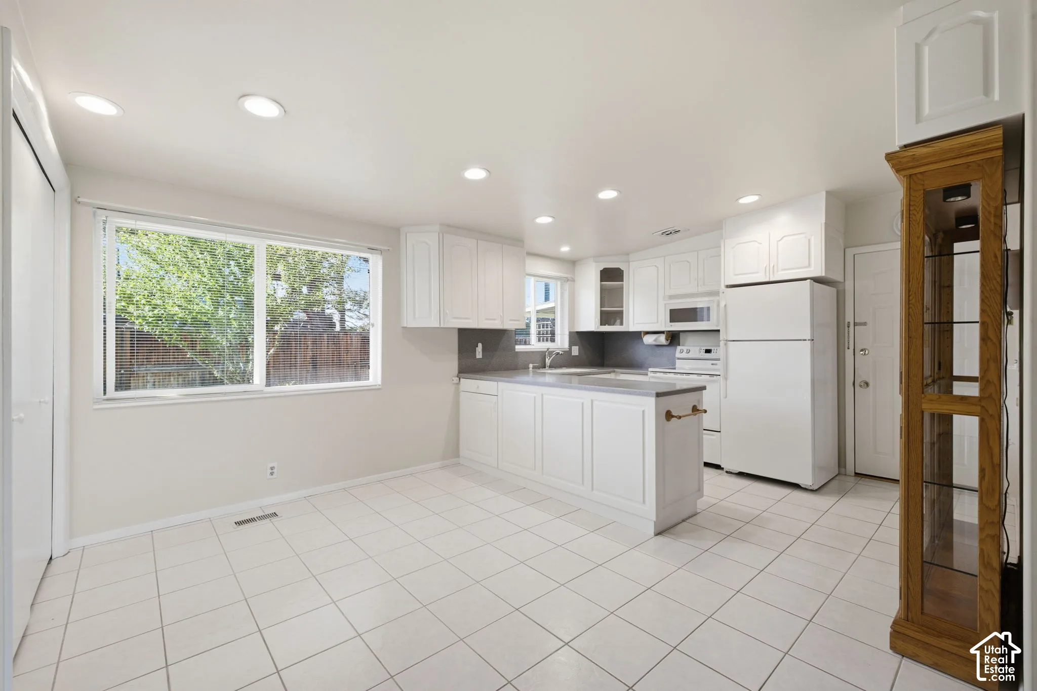 White cabinetry, light-toned tile flooring, recessed ceiling lighting, a kitchen island, and a large window