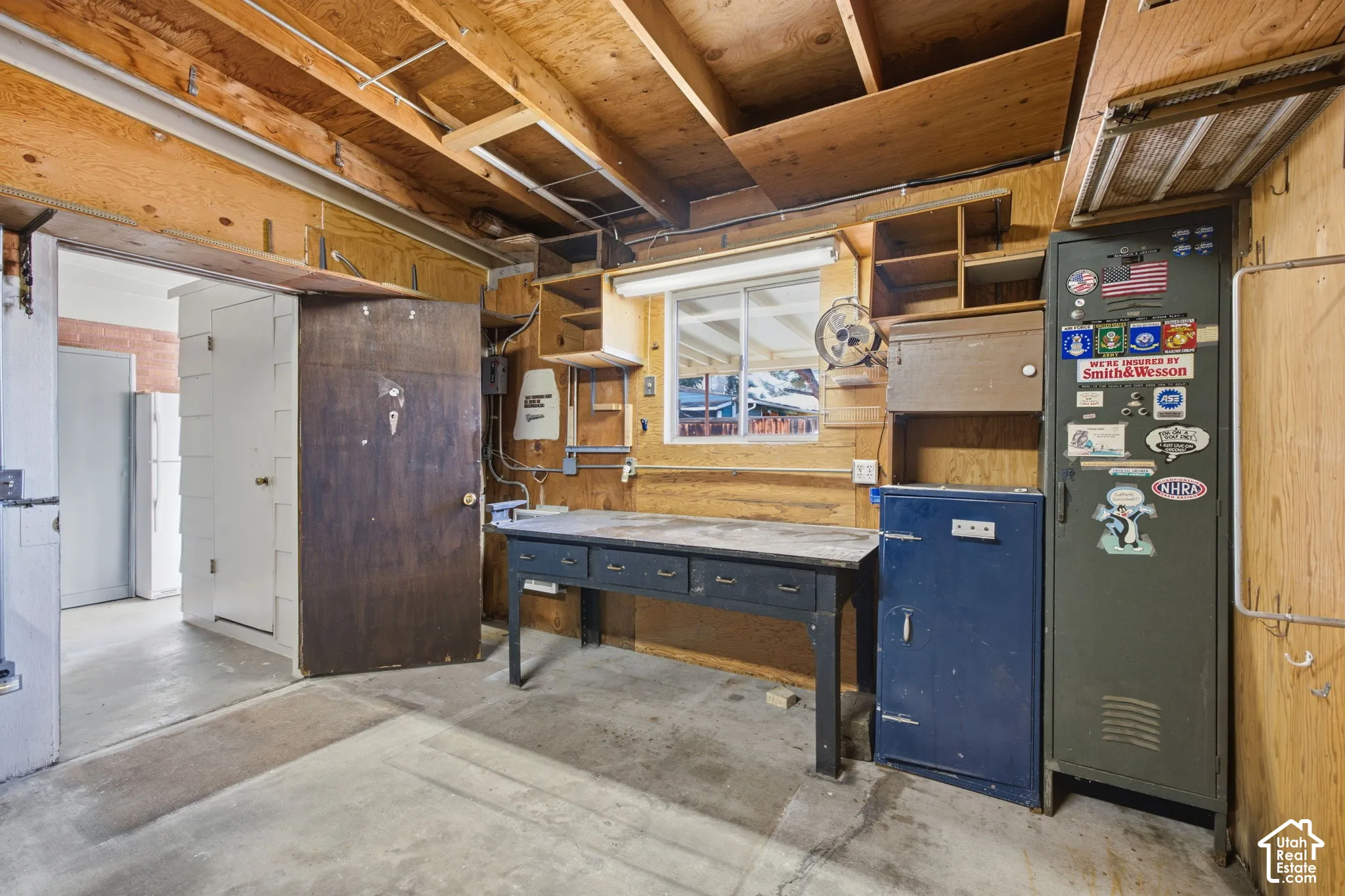Concrete flooring, exposed wood beam ceiling, wood-paneled walls, built-in shelving, and a single window
