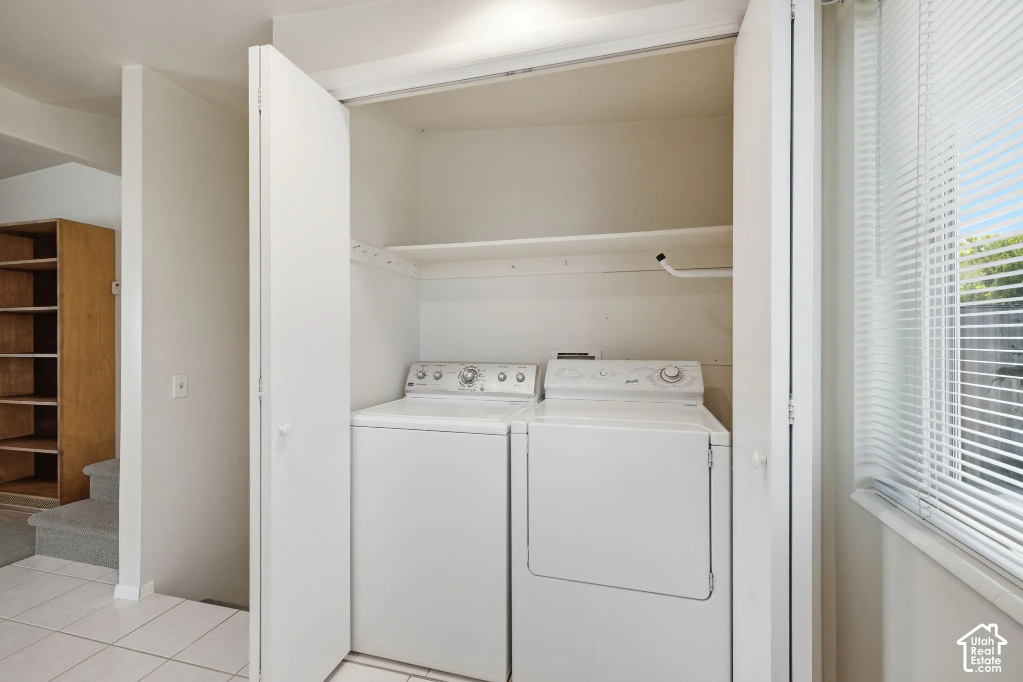 Dedicated laundry closet with built-in shelving, white appliances, and tiled flooring