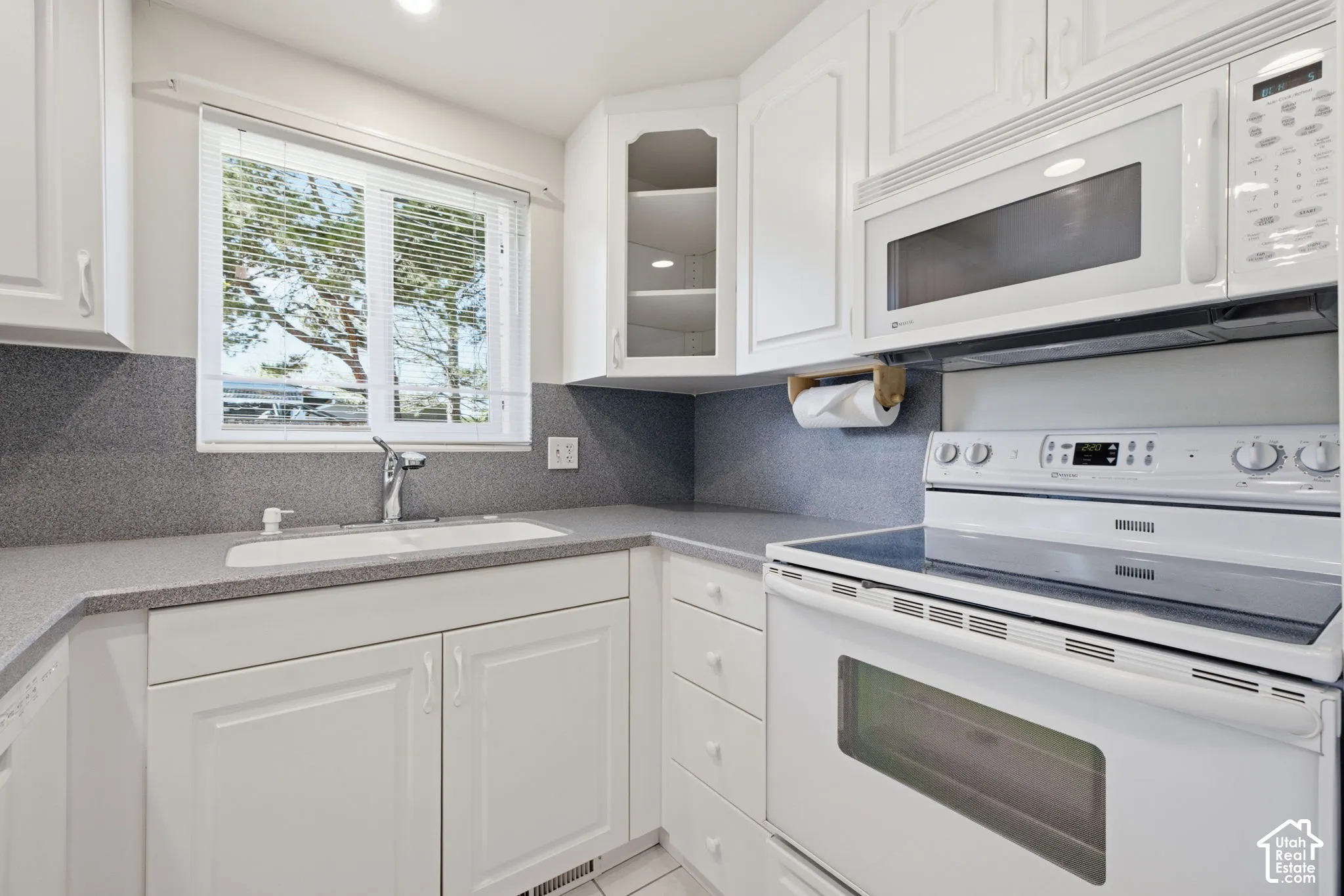White cabinetry with brushed nickel hardware, gray countertops, and a white built-in sink with a gooseneck faucet