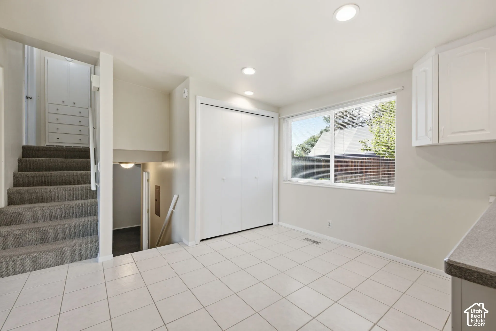 White tile flooring with a large window, white upper cabinetry, and recessed lighting